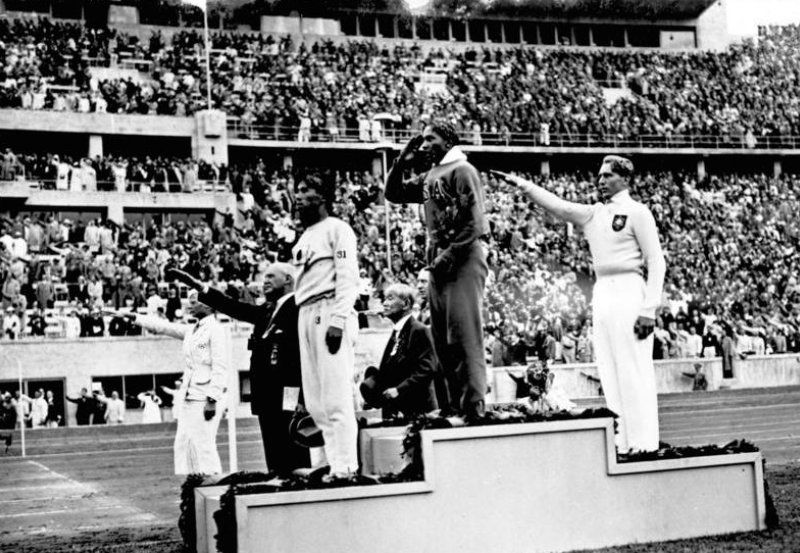 Jesse Owens en el podio olímpico después de su victoria en el salto de longitud en los Juegos Olímpicos de Berlín 1936 junto a Naoto Tajima (izquierda) y Luz Long (derecha).